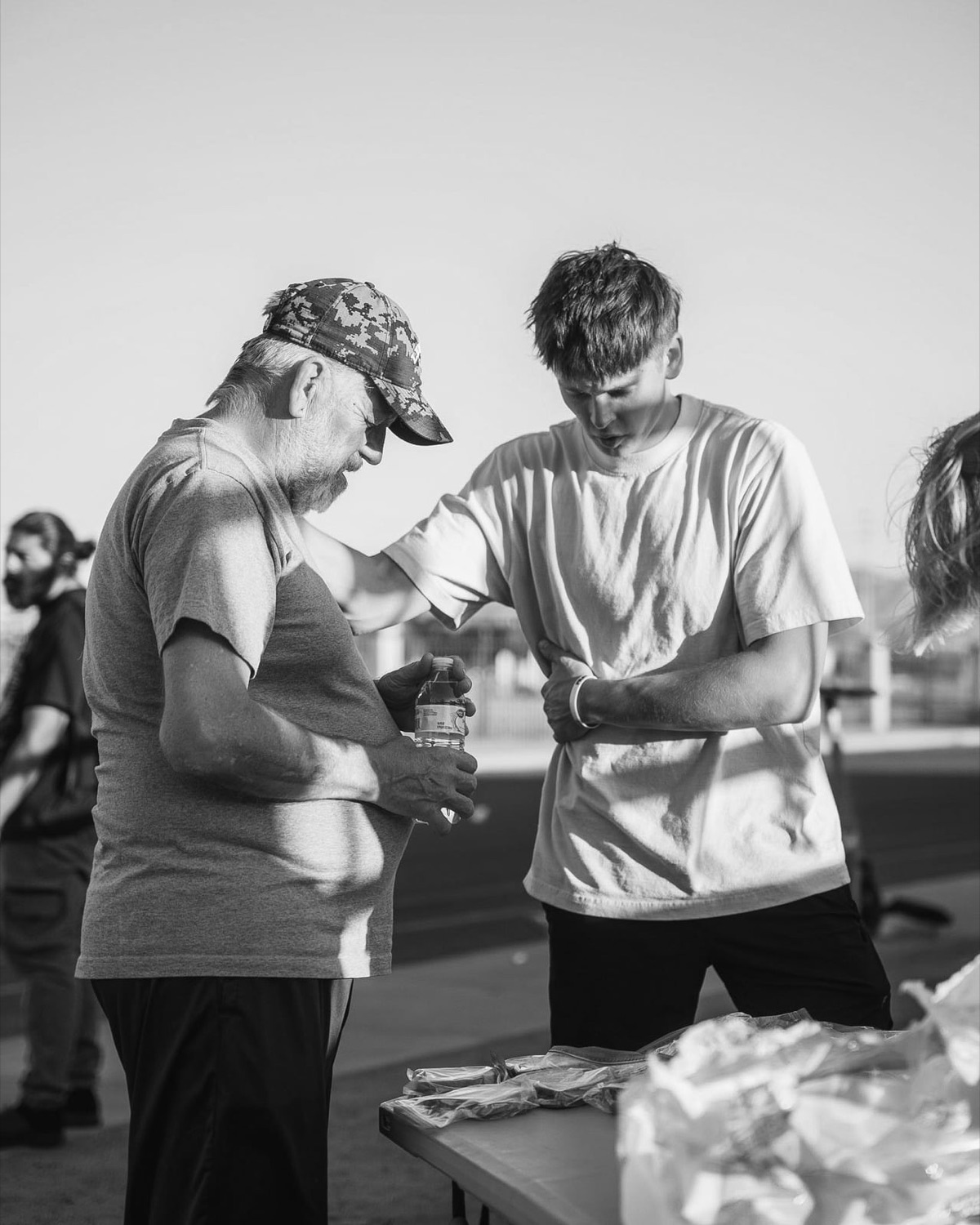 A volunteer praying with an older man holding a bottle of water