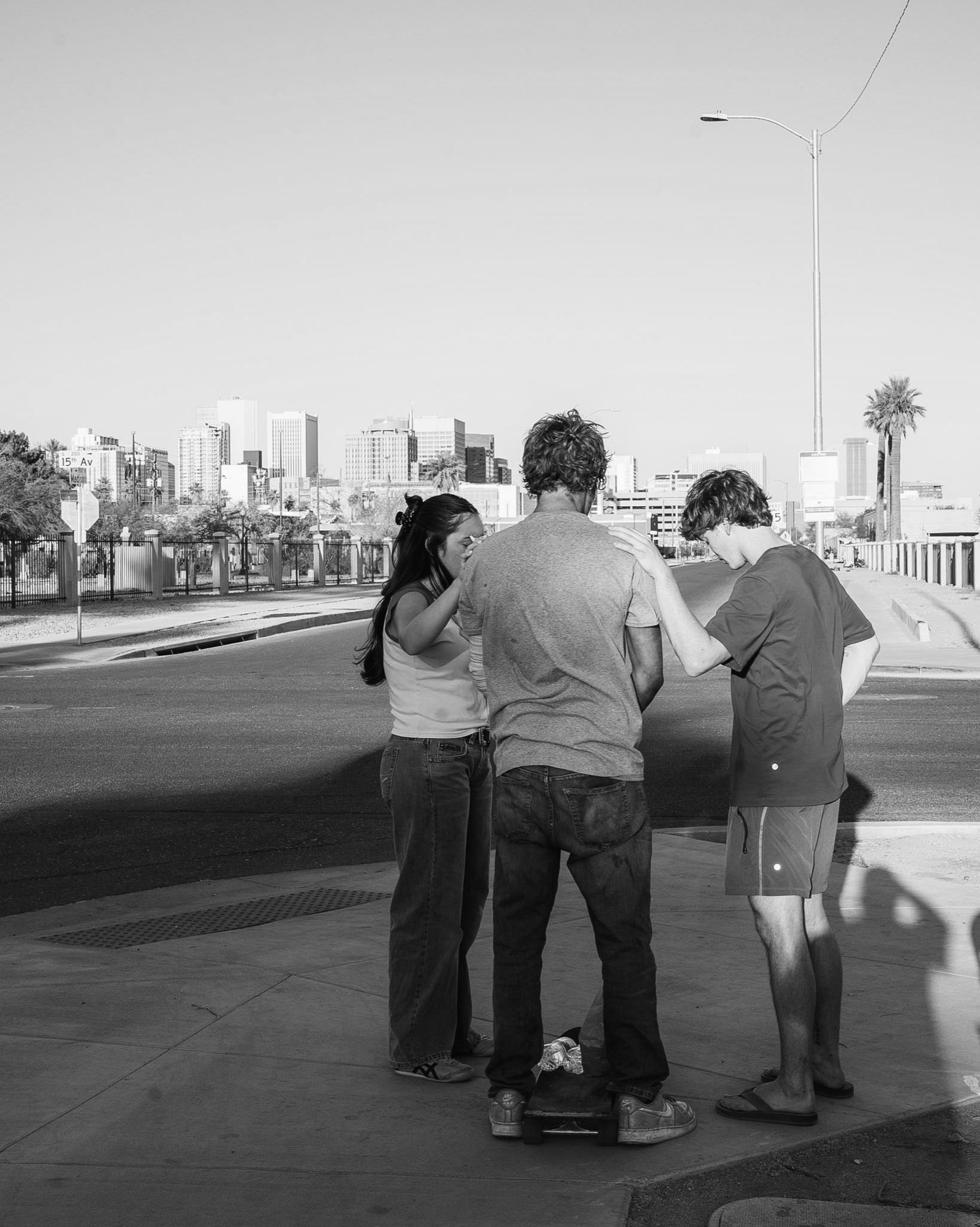 Two volunteers praying with a man on a city street, downtown skyline behind them